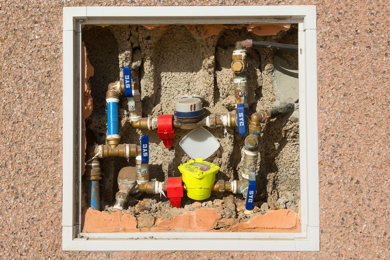 Services Detailed view of a complex water meter setup embedded in a concrete wall.