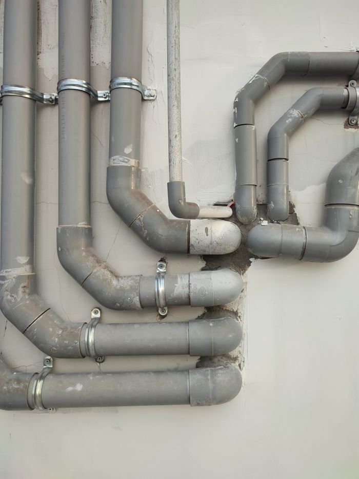 Mastering the First Impression: Your intriguing post title goes here Close-up of interconnected gray metal pipes on an outdoor wall showcasing industrial design.